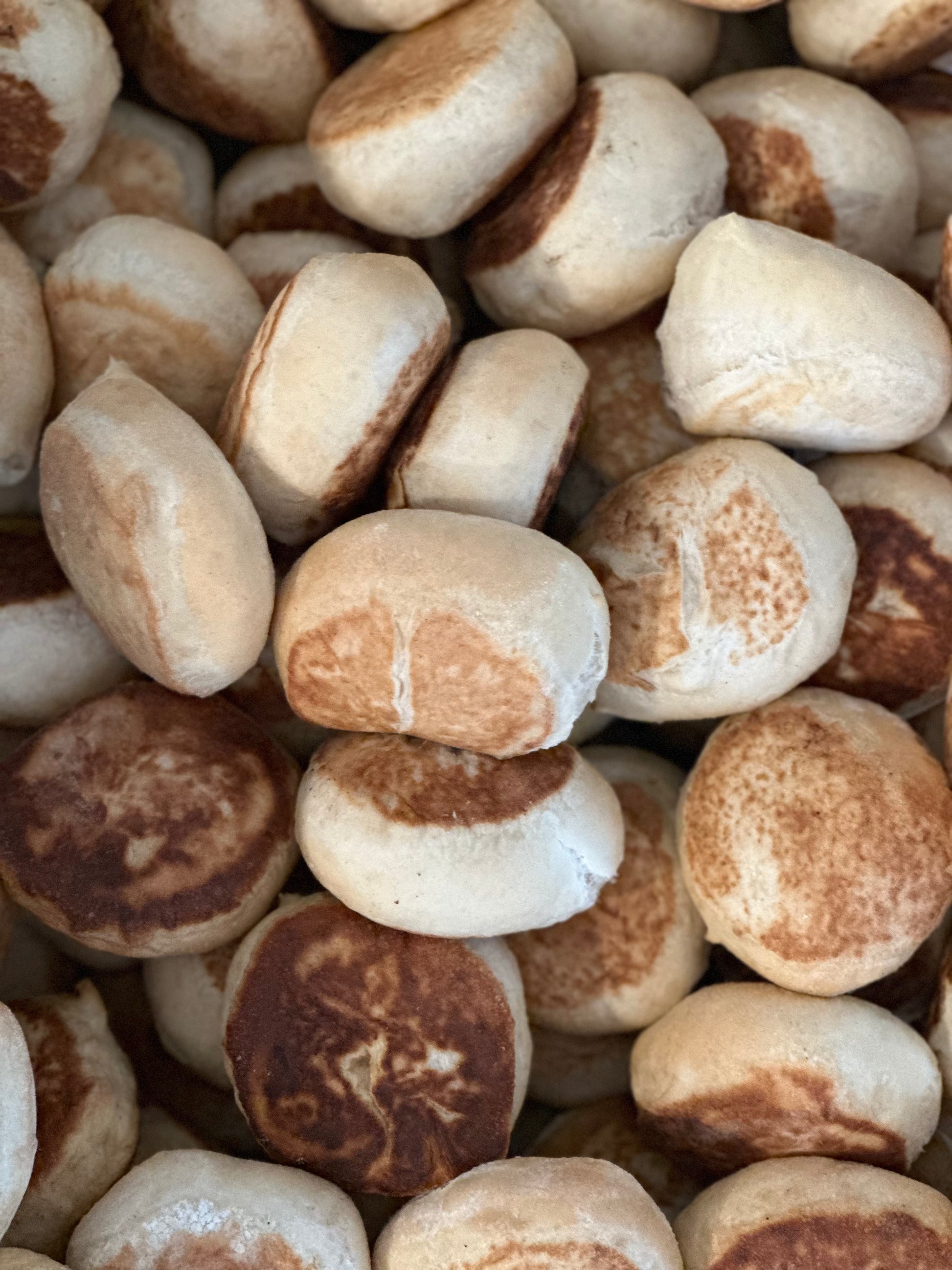A close-up of several sourdough English muffins showing their browned surfaces and textured surfaces.
