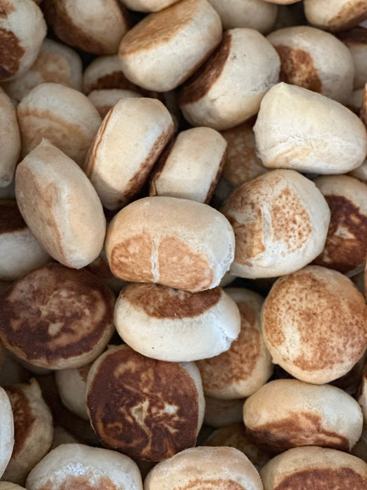 A close-up of several sourdough English muffins showing their browned surfaces and textured surfaces.